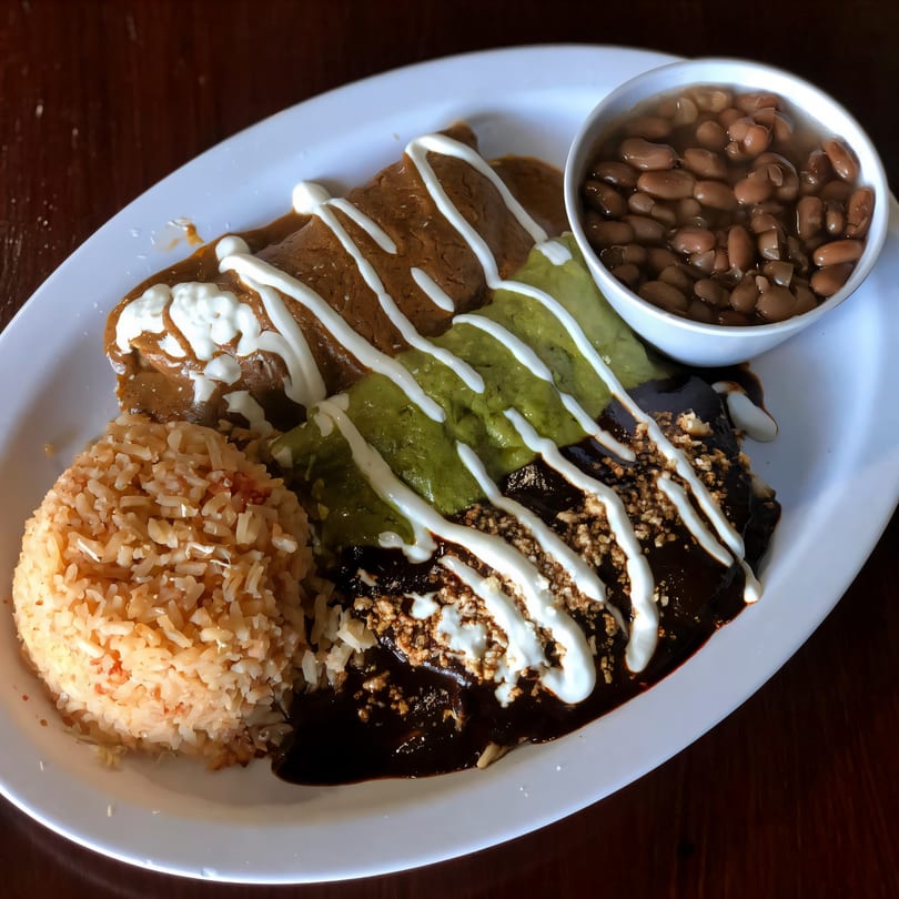 A Mexican combination plate with enchiladas, rice, and a side of beans on a white oval plate.