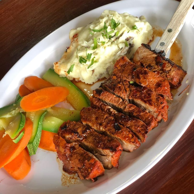 Sliced steak with mashed potatoes, carrots, and zucchini on a white plate at Teresa's Mexican Grill.